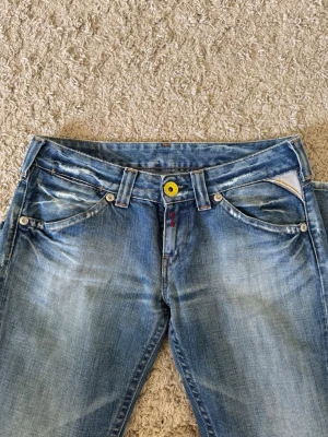 Ljusblå jeans Replay  - Säljer de här ljusblå low waist jeansen från Replay  med med gula detaljer. De är raka i benen och har en uttvättad look. Storlek W28 L30