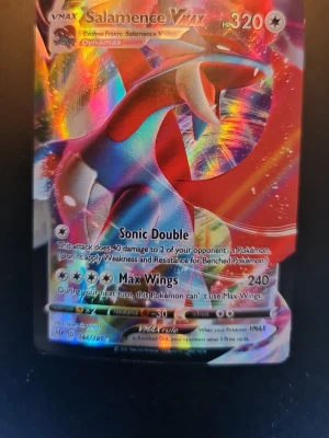 Pokémonkort Salamence VMAX 144/189 - Säljer ett Salamence VMAX Pokémonkort med holografisk yta från Sword & Shield-serien. Kortet har färgstark design med Salamence i blått, rött och vitt och attacker som Sonic Double och Max Wings. Perfekt för samlare eller Pokémon TCG-spelare.