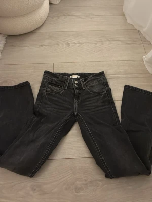 Svarta bootcut jeans med slitningar - Säljer ett par svarta bootcut jeans med lätt slitna detaljer och kontrastsömmar. Jeansen har klassisk femficksmodell och stängs med knapp och dragkedja. Materialet är denim med en något stretchig känsla. Perfekta för en avslappnad och trendig look. Dom är även lågmidjade och bootcut, från Gina Young i storlek 152.