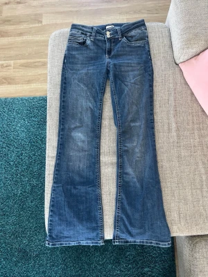 Blå bootcut jeans med broderade fickor - Säljer ett par blå bootcut jeans med snygga slitningar och broderade detaljer på bakfickorna. Säljer därav de är för stora i midjan. De är i storlek 38/short. Nypris 799kr