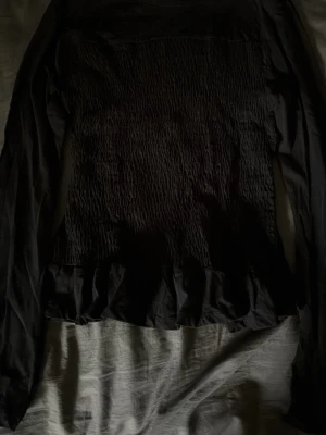 Svart långärmad topp från Gina Young - Svart långärmad topp från Gina young  Smockad front med volangdetalj. Använd 1 gång. Mjuk och stretchig.