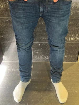 Lee jeans  - Säljer ett par blå slim fit jeans med klassisk femficksdesign och smal passform. Jeansen har normal midja och är tillverkade i ett stretchigt denimtyg som sitter tajt längs benen. Perfekta för en modern och avslappnad stil.