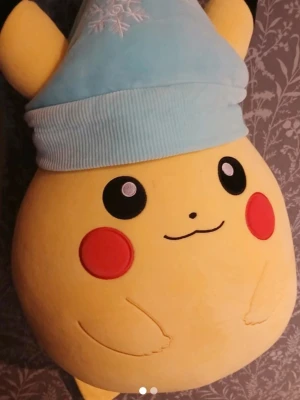 Stor Pikachu-gosedjur med blå mössa - Säljer ett stort, mjukt Pikachu-gosedjur med rund form och en ljusblå mössa med snöflingebrodyr. Gosedjuret är gult med röda kinder och svarta ögon, perfekt som prydnad eller mysig kompis. Tillverkad i plyschmaterial.