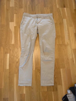 Beige chinos från Calvin Klein Jeans - Snygga beige chinos från Calvin Klein Jeans med klassisk rak passform och diskreta sidofickor. Tillverkade i ett mjukt och bekvämt material som passar perfekt till en avslappnad men stilren look. Bälteshällor och knappgylf för enkel styling.