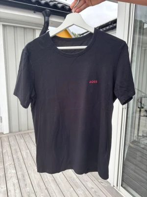 Svart t-shirt från BOSS - Snygg svart t-shirt från BOSS med diskret röd logga på bröstet. Klassisk rund halsringning och korta ärmar. Perfekt basplagg i mjuk bomull som funkar till allt. Enkel och stilren design som alltid är rätt.