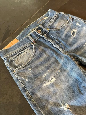 DonDup George - Säljer ett par riktigt feta Dondup jeans i modellen George. De är i en riktigt snygg blå tvätt med sjukt snygga slitningar som ger jeansen riktig karaktär. Tillverkade i Italien i 89% bomull och 11% elastan.  Storlek 30 Mått: Ytterben: 105cm, innerben: 79, Benöppning: 15cm, midja: 38cm.