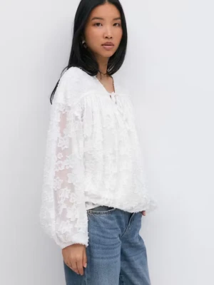 Vit blommig spetsblus med v-ringning - Söt vit blus med v-ringning och långa ärmar från Gina💞 Blusen har ett transparent lager med broderade blommor och knytband vid halsen. Materialet är tunt och luftigt, vilket gör den skön att bära.