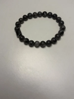 Svart pärlarmband i sten  - Snyggt armband med runda svarta pärlor av sten. Pärlorna har en matt finish och sitter på en elastisk tråd, vilket gör det enkelt att ta på och av. Perfekt accessoar för dig som gillar en stilren och minimalistisk look.