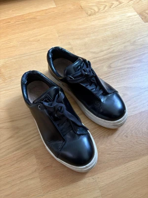 Eytys doja svarta - Snygga svarta sneakers i blankt läder med svarta skosnören och tjock vit sula. Klassisk låg modell som passar till det mesta och ger en clean look. Perfekta för dig som gillar stilrena och tidlösa skor.