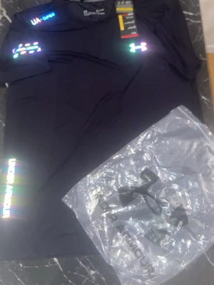 Svart träningst-shirt Under Armour - Svart kortärmad träningst-shirt från Under Armour med reflekterande logga på bröstet och ärmen. Tillverkad i ett lätt och snabbtorkande syntetmaterial som passar perfekt för träning. Levereras med originalpåse.