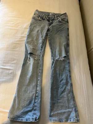 Ljusblå bootcut jeans med slitningar - Säljer ett par ljusblå bootcut jeans med slitna detaljer på båda knäna. 