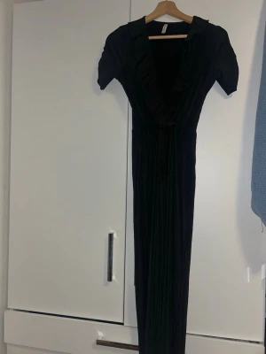 Svart jumpsuit från Stradivarius - Snygg svart jumpsuit från Stradivarius med korta ärmar och djup v-ringning. Plagget har ribbad struktur och långa, vida ben. Perfekt för dig som gillar stilrena och trendiga plagg med en twist.