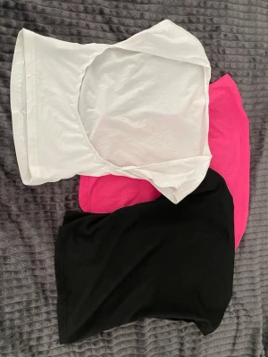 Tre basic toppar i vitt, svart och rosa - Säljer tre enkla toppar i vitt, svart och rosa. Alla har kort ärm och rund halsringning, perfekta att matcha till jeans eller kjol. Materialet känns mjukt och stretchigt, troligen bomull eller bomullsblandning. Snygga basplagg för garderoben!