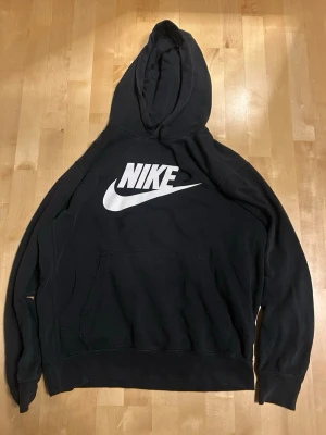Svart Nike hoodie med stor logga - Säljer en svart hoodie från Nike med stor vit logga och swoosh på bröstet. Klassisk känguruficka framtill och huva med dragsko. Perfekt för en avslappnad och sportig stil. Tillverkad i mjukt material som är skönt att bära.