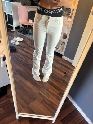 Vita bootcut jeans - Säljer ett par vita bootcut jeans med hög midja och klassisk femficksmodell. Jeansen har utsvängda ben och är tillverkade i ett stretchigt denimtyg som sitter snyggt. Perfekta för dig som vill ha en clean och fräsch look. Spretade längst ner