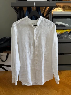 Vit linneskjorta från Massimo dutti  - Säljer en stilren vit skjorta i linne med ståkrage och knappar framtill. Skjortan har lång ärm och en avslappnad passform, perfekt för en fräsch och enkel look. Passar till både jeans och chinos.
