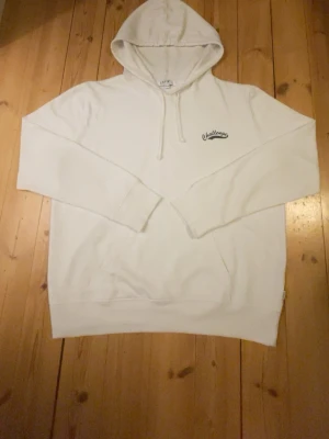 Vit hoodie med tryck Challenge - Säljer en vit hoodie med huva och dragsnören. På bröstet finns ett svart tryck med texten 'Challenge'. Hoodien har en stor magficka och ribbade muddar vid ärmar och nederkant. Perfekt för en chill och avslappnad stil.