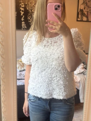 Jätte fin Vit blommig topp  - Säljer en superfin vit topp med blommigt 3D-mönster och volangdetaljer. Toppen har korta ärmar och en något boxig passform. Perfekt för dig som vill sticka ut lite extra med en unik och söt look.