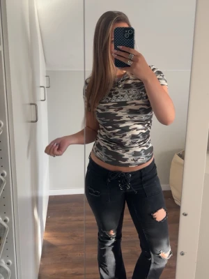 Camouflage t-shirt i tight passform - Säljer en tight, kortärmad t-shirt med grått, vitt och svart camouflage-mönster. T-shirten har rund halsringning och är i ett mjukt bomullsliknande material. Perfekt för dig som gillar streetstyle och vill sticka ut lite extra.