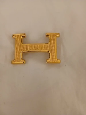 Guldfärgat H-format bältesspänne - Säljer ett stilrent bältesspänne i guldfärg format som ett H från Hermess. Spännet har en strukturerad framsida och passar perfekt till skärp med 3 cm bredd.