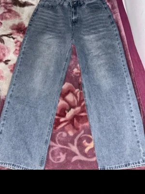 Baggy ljusblå jeans med raka ben - Säljer ett par baggy ljusblå jeans med raka, vida ben och klassisk femficksmodell. Jeansen har en avslappnad passform och är tillverkade i denim. Perfekta för en chill och trendig look.
