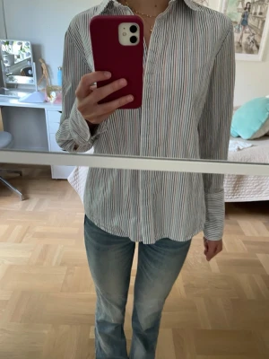 Randig skjorta från Dagmar - Säljer en klassisk skjorta från Dagmar i storlek 34. Skjortan har tunna ränder i blått, rött och turkos på vit botten, krage och långa ärmar. Tillverkad i mjuk bomull och perfekt för en clean och stilren look. Bara använd en gång därav priset men buda gärna. Djur och rökfritt hem.