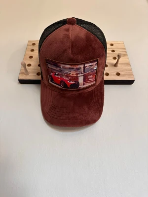 Brun keps med Cars-motiv - Säljer en rikigt fet keps med ett mäktig Ferrari motiv. Kepsen har en unik vinröd färg och passar perfekt för en avslappnad och sjysst look. 