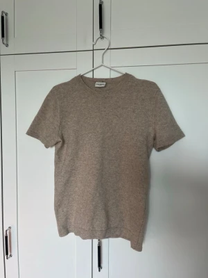 Beige kashmir t-shirt John Henric - Beige t-shirt från John Henric i mjuk kashmir. Enkel och stilren design som känns lyxig och bekväm. Perfekt för dig som gillar neutrala färger och premiumkänsla.