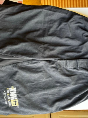 Svarta Krav maga (kampsports) shorts i junior L/ adult XS - Säljer ett par svarta Krav maga (kampsports) shorts i junior L/ adult XS. Shortsen har resår i midjan och är tillverkade i bomull. Snygga loggor på benet.