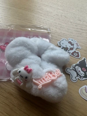 Vitt fluffigt hårband med figur - Supersöt vit fluffig scrunchie med en liten gullig figur med rosa rosett och texten 'Annabel' i rosa. Perfekt för att piffa till din frisyr med en lekfull och mjuk accessoar. Materialet är mjukt och plyschigt, vilket ger en mysig känsla.