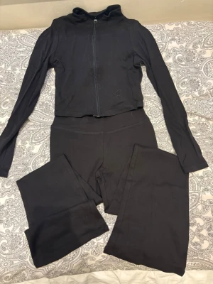 Svart set med ziptröja och tights - Säljer ett svart set från H&M med en långärmad ziptröja och matchande tights. Tröjan har hög krage och dragkedja framtill, och tightsen har hög midja. Materialet är stretchigt och mjukt, perfekt för en bekväm och stilren look.