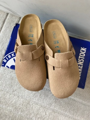 Beige Birkenstock Boston sandaler 38 - Snygga beige Birkenstock Boston sandaler i mocka med klassisk slip-in design och justerbart spänne på sidan. Mjuka innersulor och robust yttersula för skön komfort. Perfekta för en avslappnad och trendig stil.
