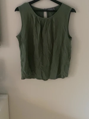 Grön ärmlös linnetopp - Snygg grön linnetopp med rund halsringning och veckad detalj framtill. Toppen är ärmlös och har en enkel, avslappnad passform som passar perfekt till sommaren. Enkel att matcha med både jeans och kjol.