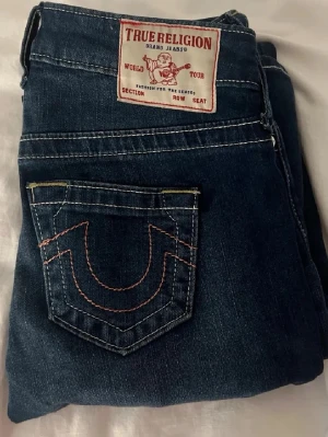 True Religion jeans - Säljer ett par super fina True Religion jeans med rosa detaljer på bakfickorna. Har sprättat upp dom längst ner för att få dom lite längre, men annars är dom i väldigt fint skick. Pris går att diskutera💞