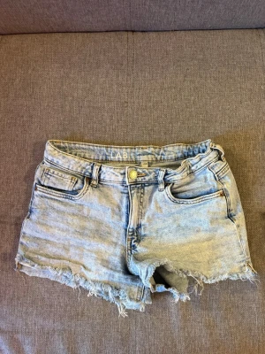 Ljusblå jeansshorts med fransar - Säljer ett par ljusblå jeansshorts med fransig kant och femficksdesign.