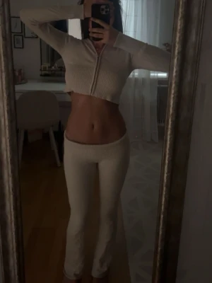 Beige ribbat loungewear-set - Säljer ett beige stickat set med croppad ziptröja och matchande byxor. Tröjan har långa ärmar och dragkedja framtill, byxorna är höga i midjan och raka i modellen. Materialet är ribbstickat och mjukt, perfekt för en chill och trendig look. Tröjan är i strl 164/XS och byxorna i strl 170/S.
