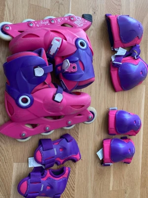 Rosa och lila inlines med skydd - Säljer ett set med rosa och lila inlines från Oxelo i storlek 34-36. Medföljer matchande skydd för knän, armbågar och handleder. Perfekt för dig som vill åka säkert och snyggt! Allt har cool design och justerbara spännen.