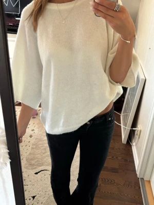 Vit oversized stickad tröja - Säljer en vit oversized stickad tröja med trekvartsärmar och rund halsringning. Tröjan har en avslappnad passform och är gjord i ett mjukt, tunt stickat material. Perfekt att styla med jeans eller kjol för en chill look.