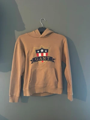 Gant hoodie  - Säljer en gant hoodie som är väldigt fint skick och är beige/brun färgad. Den passar på 13/14 åringar, och 154-164 cm så det är alltså storlek XS. Hör av er om ni har frågor, eller pris😃✅