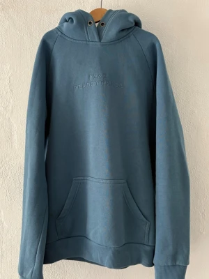 Blå hoodie från Peak Performance - Snygg blå hoodie från Peak Performance med broderad logga på bröstet. Hoodien har huva med dragsko, känguruficka framtill och ribbade muddar vid ärmslut och nederkant. 