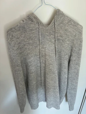 Ljusgrå cashmere hoodie - Ljusgrå stickad hoodie med huva och dragsko. Tröjan har en enkel och stilren design utan tryck eller logga, och är tillverkad i ett mjukt material som känns skönt mot huden. Perfekt för dig som gillar en avslappnad och clean look.