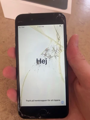 Svart iPhone med sprucken skärm - Säljer en svart iPhone med klassisk rund hemknapp och glasfront. Telefonen har en elegant, slimmad design i metall och glas. Perfekt för dig som gillar Apples stilrena look och vill ha en smidig mobil i fickan.