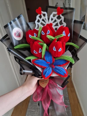 Handgjord spidermanbukett med  - Unik handgjord spiderman- bukett med röda och blå piprenar-blommor, gröna blad och dekorativa vita detaljer. Buketten är inslagen i svart och transparent plast med rosa band och små hjärtan. Perfekt som present eller dekoration. 