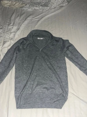 Grå halvzip tröja från RYVLS - Snygg grå stickad tröja från RYVLS med halvzip och hög krage. Perfekt för lager på lager och enkel att matcha med olika outfits. Tröjan har långa ärmar och ribbade muddar vid ärmslut och nederkant. Klassisk och stilren design.