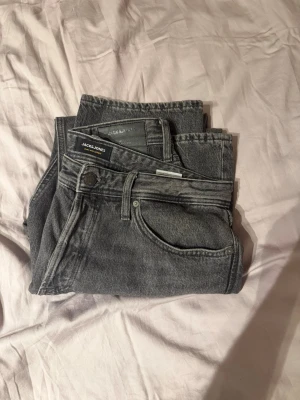Grå jeans från Jack & Jones - Säljer ett par snygga grå jeans från Jack & Jones i klassisk femficksmodell. Jeansen har raka ben och är tillverkade i slitstarkt denimtyg. Perfekta för dig som gillar en stilren och avslappnad look.