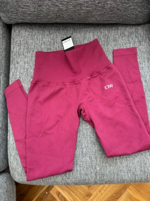 Mörkrosa seamless leggings ICANIWILL - Säljer ett par mörkrosa seamless leggings från ICANIWILL med hög midja och ribbad struktur. Stretchigt material som sitter skönt och formar sig efter kroppen. Perfekta för träning eller chill. Diskret logga på låret och bred linning för extra stöd.