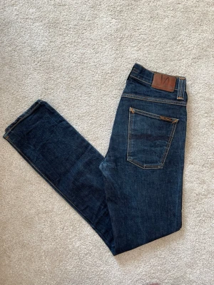 Mörkblå jeans ifrån Nudie Jeans  - Ett par riktigt feta jeans ifrån märket Nudie Jeans. Storleken är 32-34 och modellen är Grim Tim. Jeansen har en snygg passform utan defekter! Ifall du vill ha fler bilder så skriv!  😁✌🏼 ——————————————————————————                                                                      📐| Storlek: 32-34                                                  👖| Märke: Nudie jeans                                         🔎| Skick: Fint skick!                                               💵| Ny Pris: 1699kr