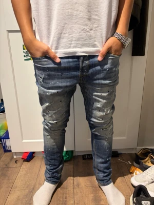 Jack and Jones jeans med slitningar  - Säljer ett par blå slim fit jeans med coola slitningar och färgstänk för en trendig look. Jeansen har klassisk femficksdesign och smal passform som sitter snyggt längs benen. Perfekta för dig som gillar streetwear och vill sticka ut lite extra.