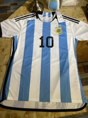 Argentina fotbollströja nr 10 - Säljer en klassisk Argentina fotbollströja med vertikala blå och vita ränder, svarta detaljer och nummer 10 på bröstet. Tröjan har rund hals, korta ärmar och AFA-emblemet på vänster sida. Perfekt för dig som älskar fotboll och vill stötta ditt lag.