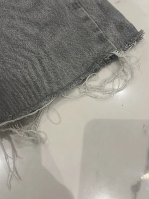 Grå jeans med rå kant från Zara - Säljer ett par grå jeans från Zara med snygg rå kant nertill och klassisk femficksmodell. Jeansen har hög midja och är i ett mjukt bomullsmaterial. Perfekta för en avslappnad och trendig look.